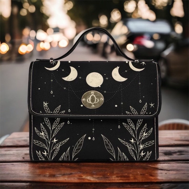 May include: A black handbag with a moon and stars design. The bag has a gold clasp and a top handle.
