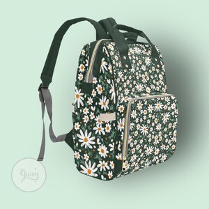 Peut inclure: Un sac &agrave; langer vert fonc&eacute; avec un imprim&eacute; floral de marguerites blanches. Le sac a plusieurs poches et une fermeture &eacute;clair.