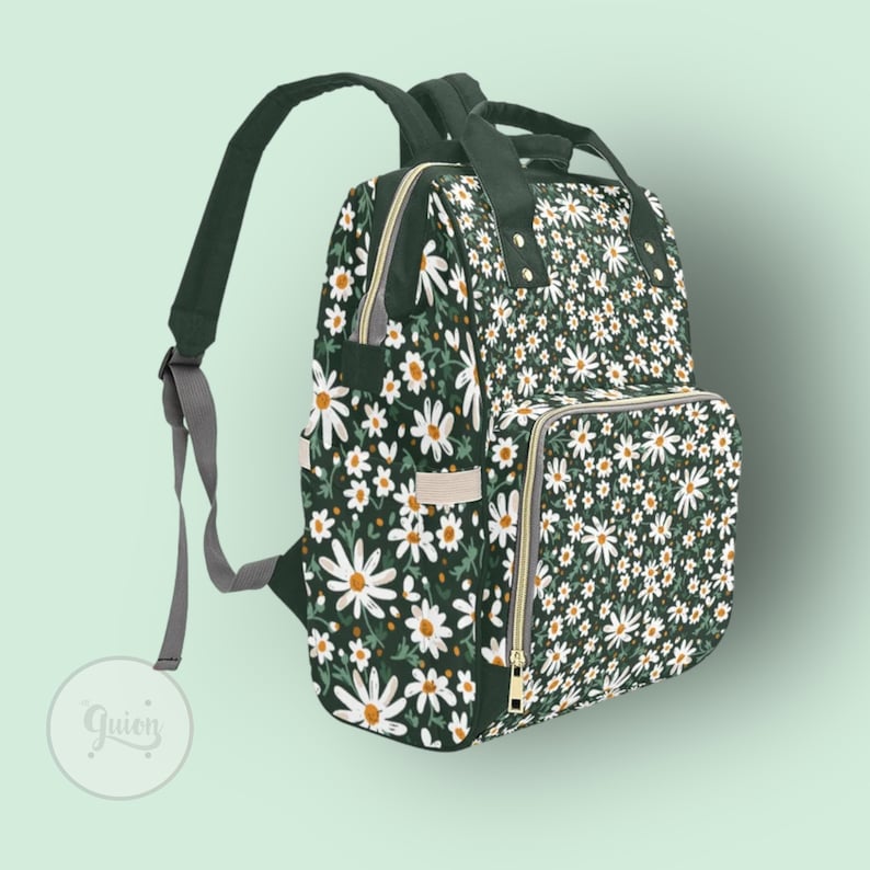 Peut inclure: Un sac &agrave; langer vert fonc&eacute; avec un imprim&eacute; floral de marguerites blanches. Le sac a plusieurs poches et une fermeture &eacute;clair.