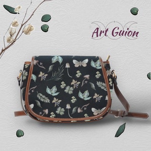 Puede incluir: Un bolso de montar negro con ribete de cuero marr&oacute;n y una correa para el hombro. El bolso tiene un estampado floral con setas, mariposas y hojas.