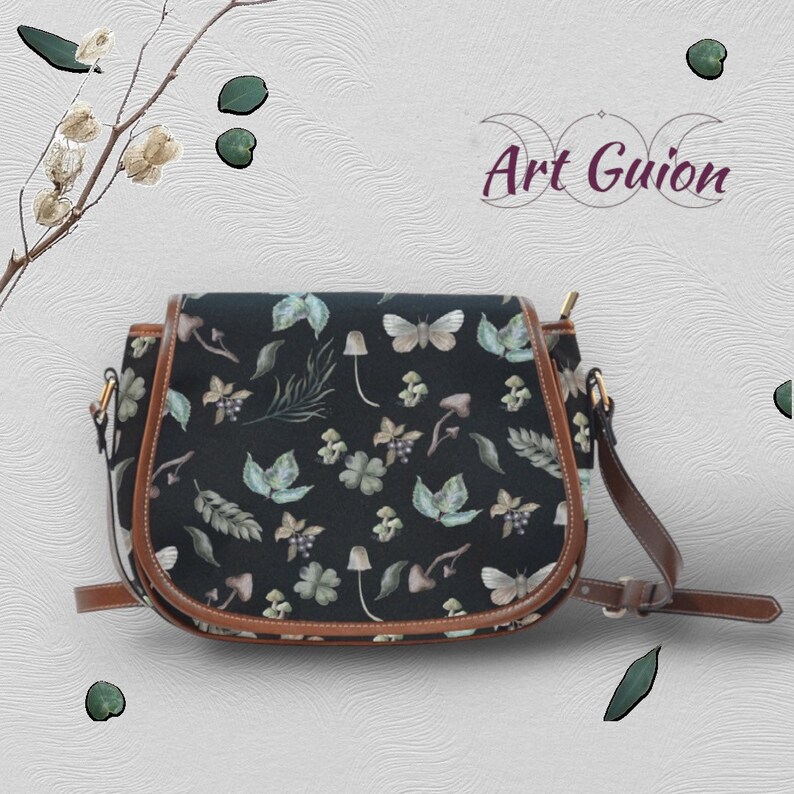 Puede incluir: Un bolso de montar negro con ribete de cuero marr&oacute;n y una correa para el hombro. El bolso tiene un estampado floral con setas, mariposas y hojas.