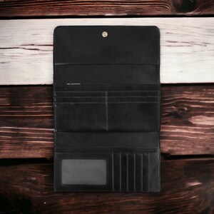 May include: A black leather wallet with multiple card slots and a clear ID window. The wallet is open and laid flat on a wooden surface.