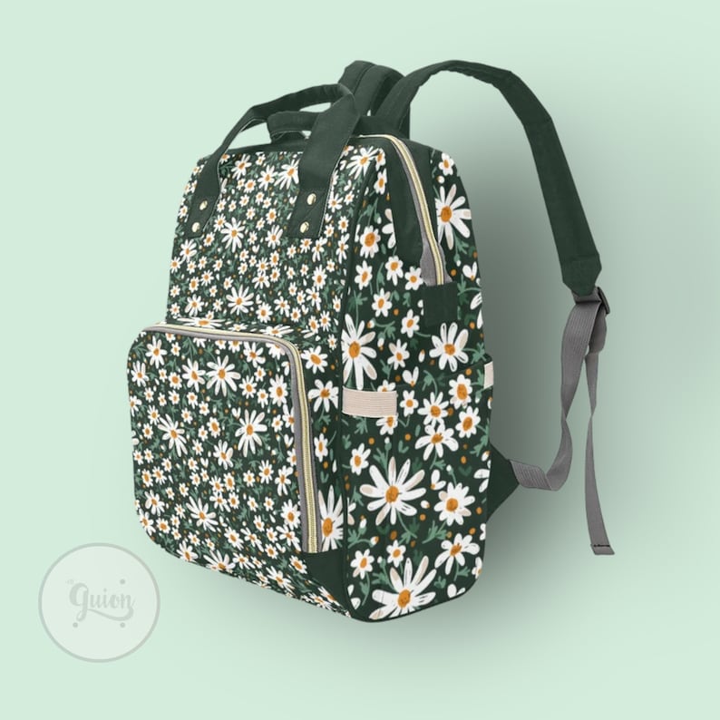 Peut inclure: Un sac &agrave; dos vert fonc&eacute; avec un motif floral de marguerites blanches. Le sac &agrave; dos a une poche avant zipp&eacute;e et des bretelles r&eacute;glables.