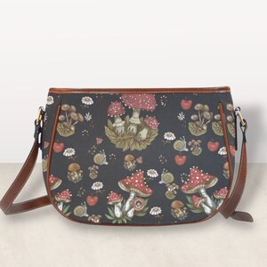 May include: A black leather shoulder bag with a brown trim and a mushroom print. The print features red and white mushrooms with green leaves and stems.