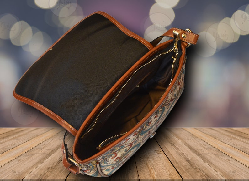 Puede incluir: Un bolso de hombro de cuero marr&oacute;n y lona con cierre de cremallera y dise&ntilde;o estampado. El bolso est&aacute; abierto y el interior est&aacute; forrado con tela negra.