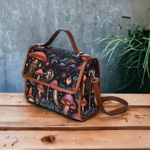 May include: A brown leather satchel handbag with a shoulder strap. The bag has a black fabric lining with a colorful mushroom and floral pattern.