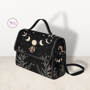 May include: A black satchel handbag with a gold clasp and a long adjustable strap. The bag features a celestial design with moons and stars in a white outline.