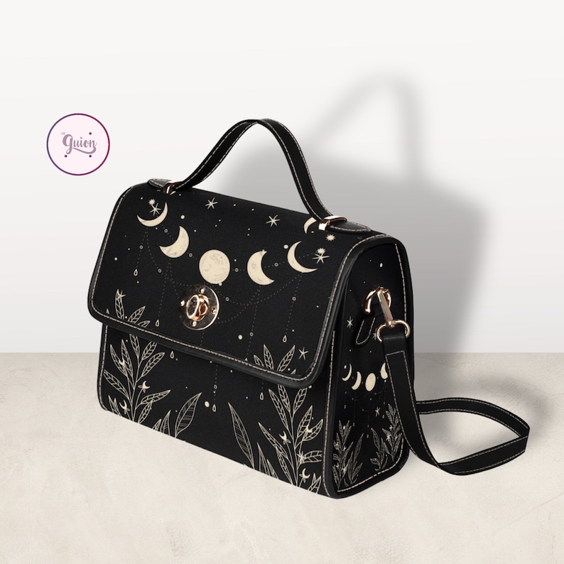 May include: A black satchel handbag with a gold clasp and a long adjustable strap. The bag features a celestial design with moons and stars in a white outline.