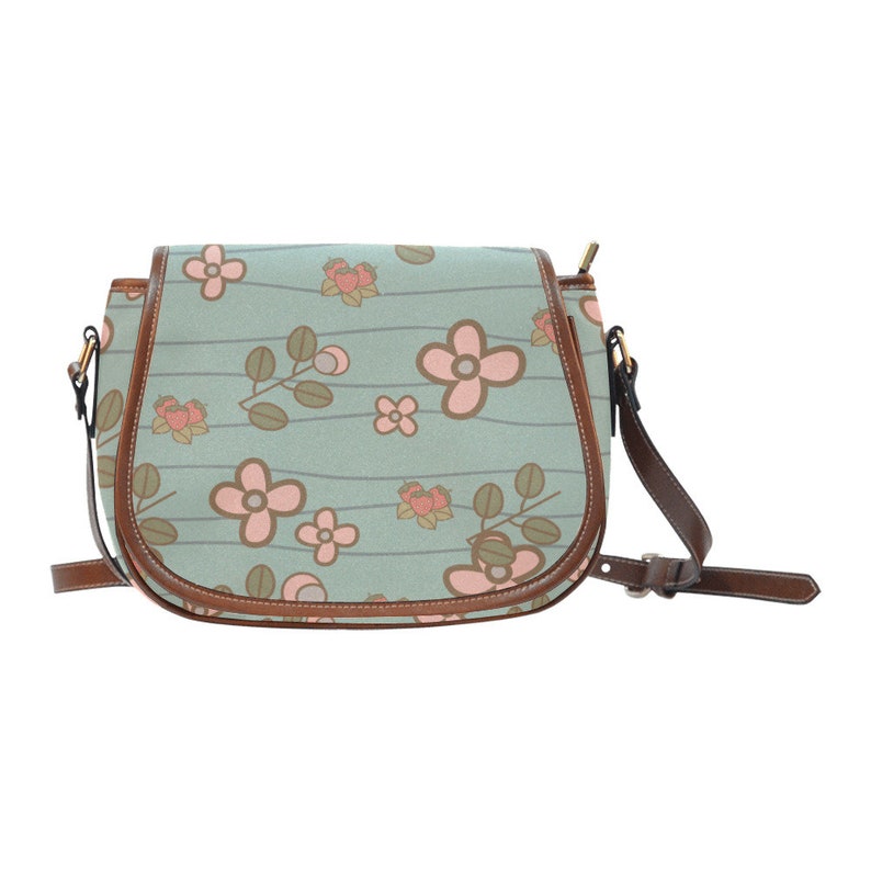 May include: A floral-patterned crossbody bag with a light blue background and brown trim. The bag features a repeating pattern of pink flowers and green leaves. The adjustable strap and flap closure are brown.