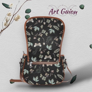 Puede incluir: Un bolso bandolera de cuero marr&oacute;n con cierre de solapa. El bolso tiene un forro de tela negro con un estampado floral con mariposas, hojas y setas.