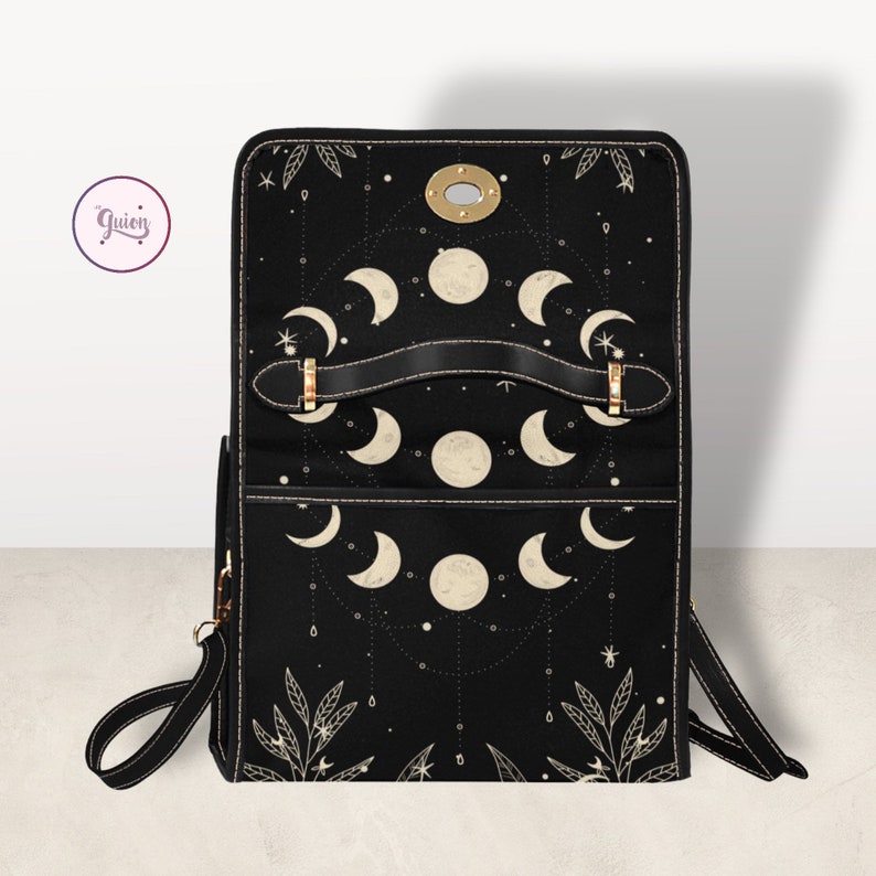 May include: Black leather backpack with a moon and stars design. The backpack has a flap closure with a gold buckle and a top handle.