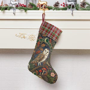 May include: A Christmas stocking with a detailed owl and forest design. The stocking features a plaid cuff in red and green, with a dark blue background. The owl is the focal point, surrounded by mushrooms, flowers, and a hedgehog. The stocking is hanging from a white mantel.