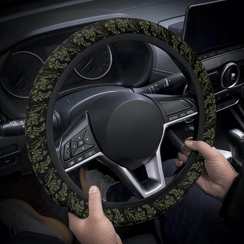 May include: A black steering wheel cover with a green and black floral pattern. The cover is made of a soft, comfortable material and is designed to improve grip and comfort while driving.