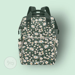 Peut inclure: Un sac &agrave; langer vert fonc&eacute; avec un imprim&eacute; de marguerites blanches. Le sac a plusieurs poches et une fermeture &agrave; glissi&egrave;re.