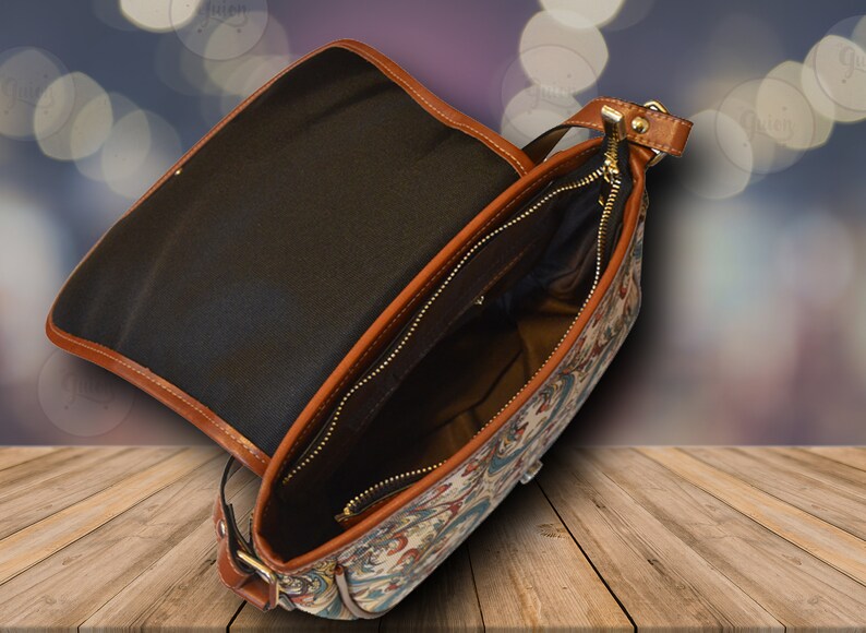 May include: A brown leather and canvas shoulder bag with a zipper closure and a patterned design. The bag is open and the inside is lined with black fabric.