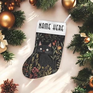May include: A Christmas stocking with a black cat design. The stocking features a black cat illustration surrounded by colorful flowers and foliage on a black background. The top of the stocking has the text "NAME HERE" in white.