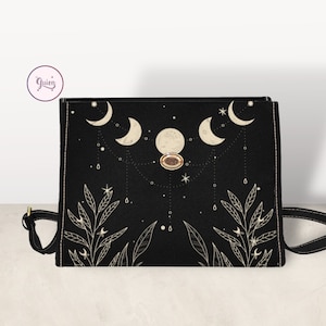 May include: Black canvas crossbody bag with a gold button closure. The bag features a design of crescent moons, stars, and leaves in a cream color.