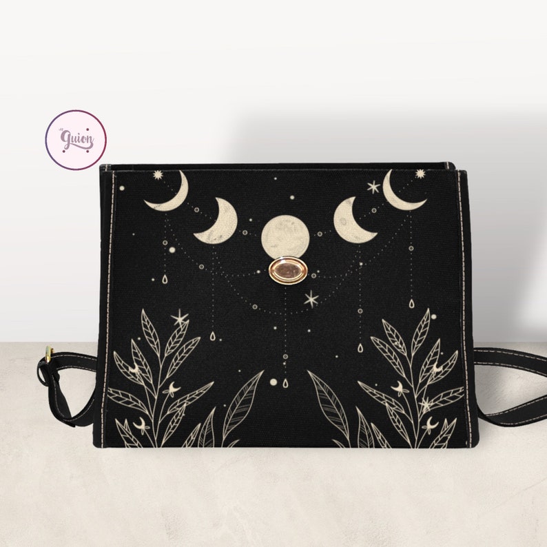 May include: Black canvas crossbody bag with a gold button closure. The bag features a design of crescent moons, stars, and leaves in a cream color.