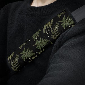 May include: A black car seatbelt cover with a repeating pattern of green ferns and white stars and crescent moons.