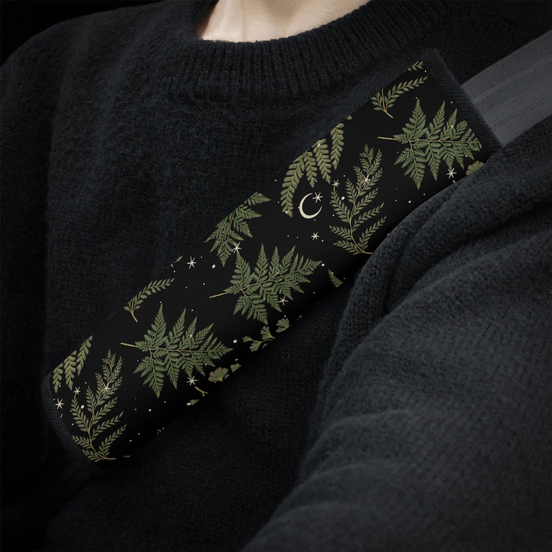 May include: A black car seatbelt cover with a repeating pattern of green ferns and white stars and crescent moons.