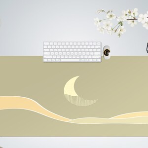 Pu&ograve; includere: Un tappetino da scrivania verde chiaro con un design a forma di luna crescente bianca e linee ondulate. Il tappetino ha un bordo giallo chiaro e un sottile motivo a onde.