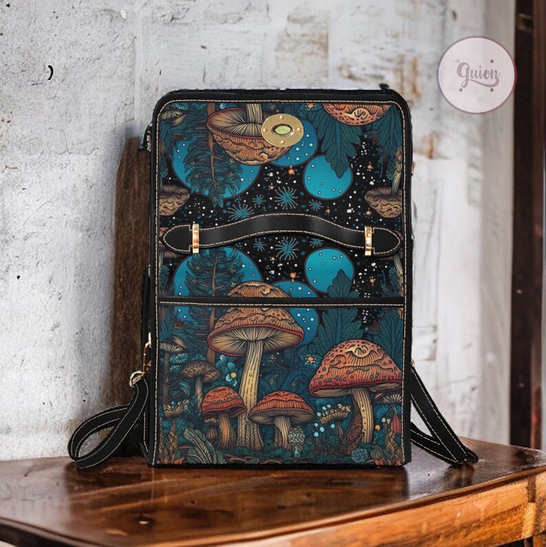 May include: A black leather backpack featuring a colourful mushroom and forest scene design. The backpack has two adjustable straps and a top handle.