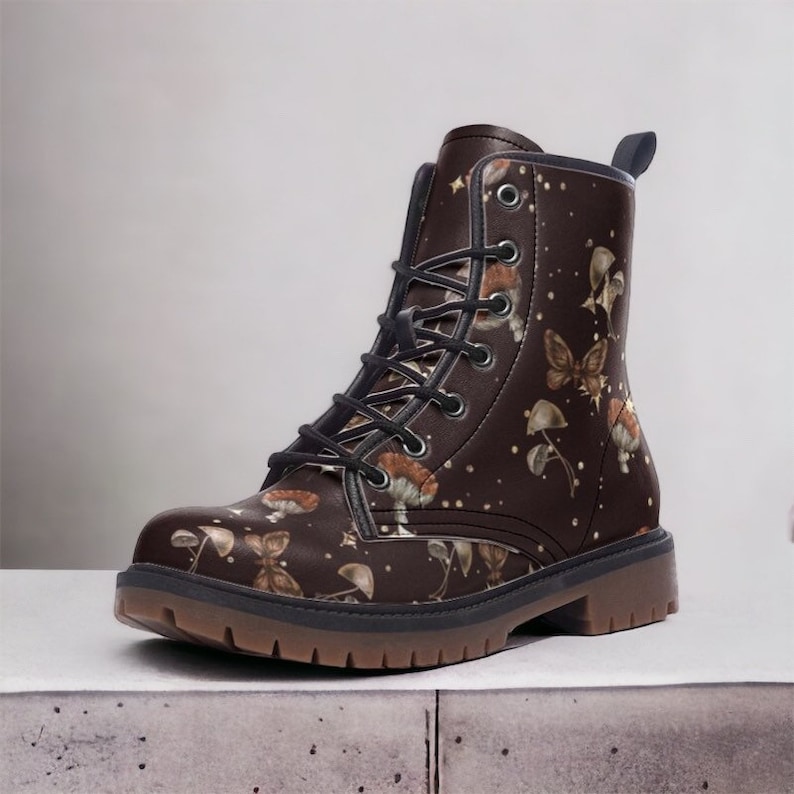 May include: Brown leather lace-up boots with a mushroom and butterfly print. The boots have a black sole and a rounded toe.