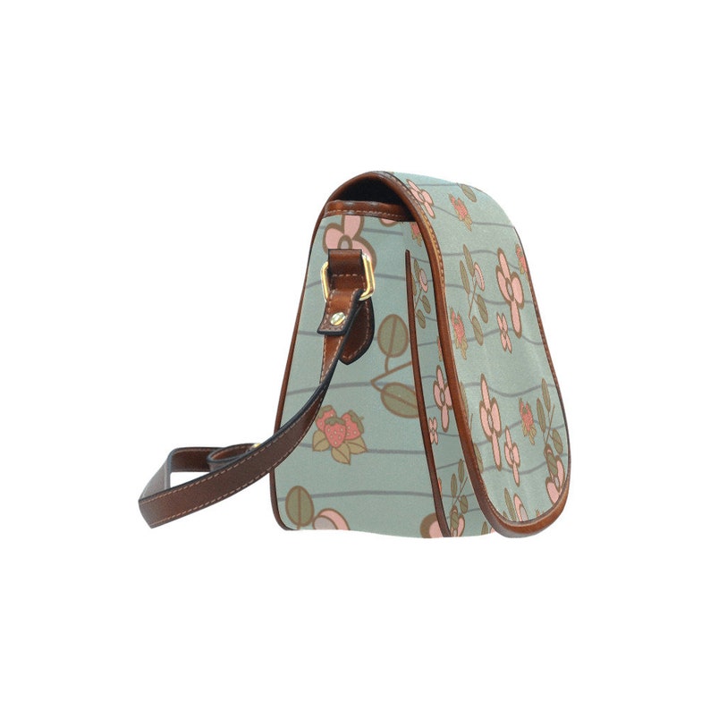 May include: A light blue crossbody bag with a floral pattern. The bag features a repeating design of pink flowers and green leaves on a striped background. It has brown leather trim, a brown strap, and a gold-colored buckle.