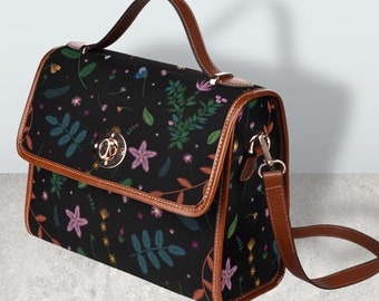 May include: A black satchel handbag with a floral pattern and brown leather trim. The bag has a top handle and a long adjustable shoulder strap.