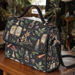 May include: A black satchel bag with a long adjustable strap. The bag has a dark green, black, and brown floral print with images of books, bottles, and mushrooms. The bag has a gold metal clasp.