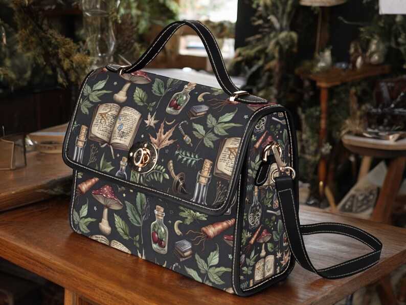 May include: A black satchel bag with a long adjustable strap. The bag has a dark green, black, and brown floral print with images of books, bottles, and mushrooms. The bag has a gold metal clasp.