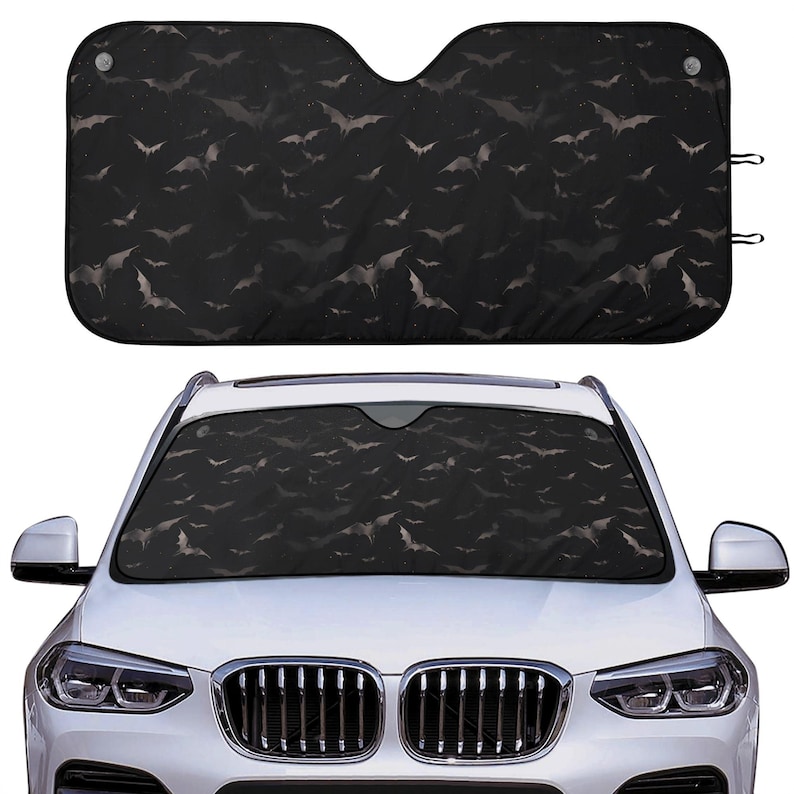 Pode incluir: Um protetor solar para carro preto com um padr&atilde;o de morcegos em um fundo escuro. O protetor solar &eacute; projetado para se ajustar ao p&aacute;ra-brisa de um carro.