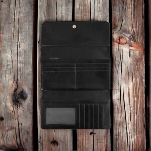 May include: A black leather wallet with multiple card slots and a billfold. The wallet is closed and lying on a wooden surface.