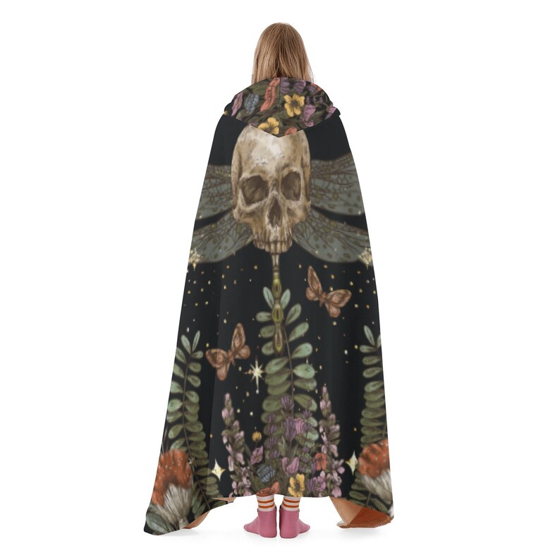 May include: Black hooded cloak featuring a skull with dragonfly wings, butterflies, and botanical elements. The cloak has a dark background with stars and floral accents. The design includes shades of brown, green, purple, and yellow.