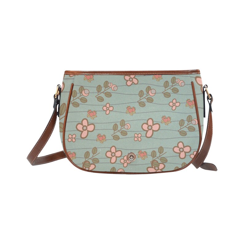 May include: A light blue crossbody bag with a floral pattern. The bag features pink flowers and brown stems against a light blue background with horizontal lines. It has a brown leather strap and trim.