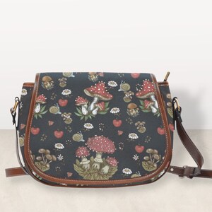 May include: A black leather satchel with a brown leather trim and a shoulder strap. The bag features a repeating pattern of red and white mushrooms, green leaves, and white flowers.