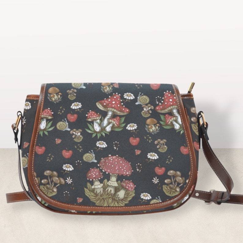 May include: A black leather satchel with a brown leather trim and a shoulder strap. The bag features a repeating pattern of red and white mushrooms, green leaves, and white flowers.