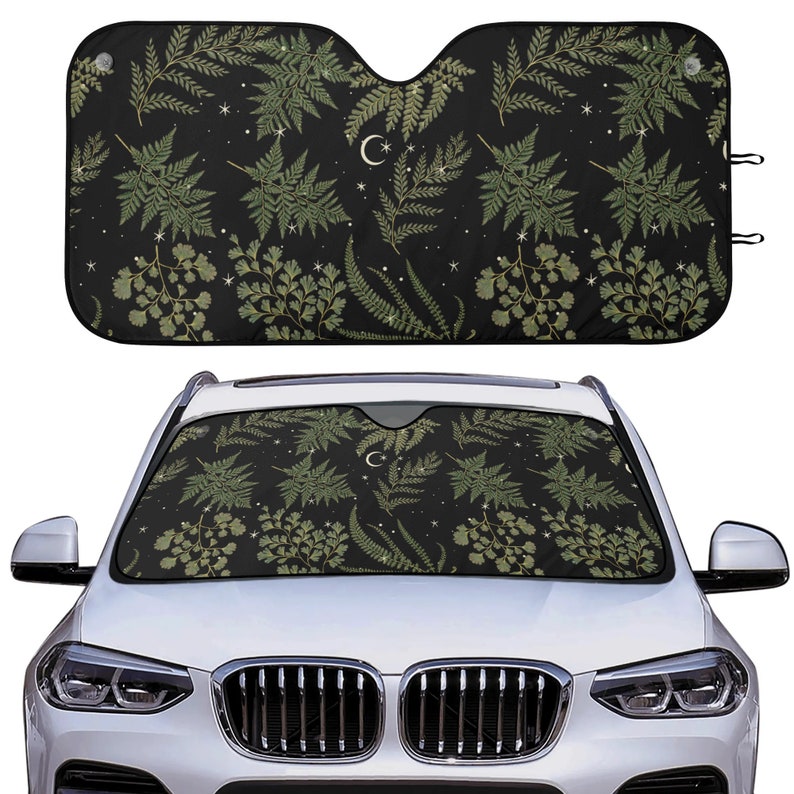 May include: A black car sunshade with a pattern of green ferns and white crescent moons on a black background.