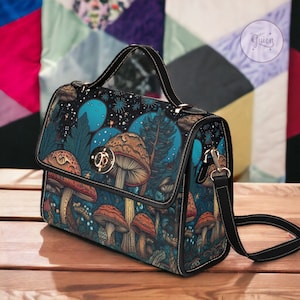 May include: A black satchel handbag with a mushroom and forest scene print. The bag has a top flap with a gold clasp and a detachable shoulder strap.