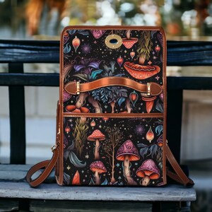 May include: A brown leather backpack with a black canvas front featuring a colorful mushroom and floral pattern. The backpack has a top flap with a metal buckle and a brown leather strap.