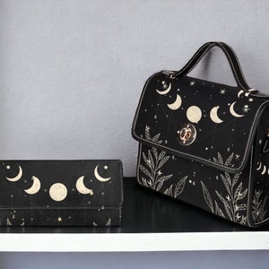 May include: A black leather handbag and matching wallet with a celestial moon and star design. The bag has a top handle and a long shoulder strap.