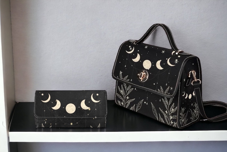 May include: A black leather handbag and matching wallet with a celestial moon and star design. The bag has a top handle and a long shoulder strap.