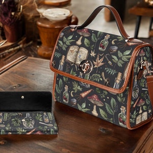 May include: A brown leather satchel with a black and green floral print featuring mushrooms, herbs, and potion bottles. The bag has a top handle and a long adjustable shoulder strap.