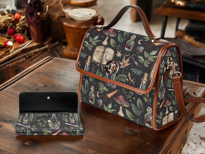 May include: A brown leather satchel with a black and green floral print featuring mushrooms, herbs, and potion bottles. The bag has a top handle and a long adjustable shoulder strap.