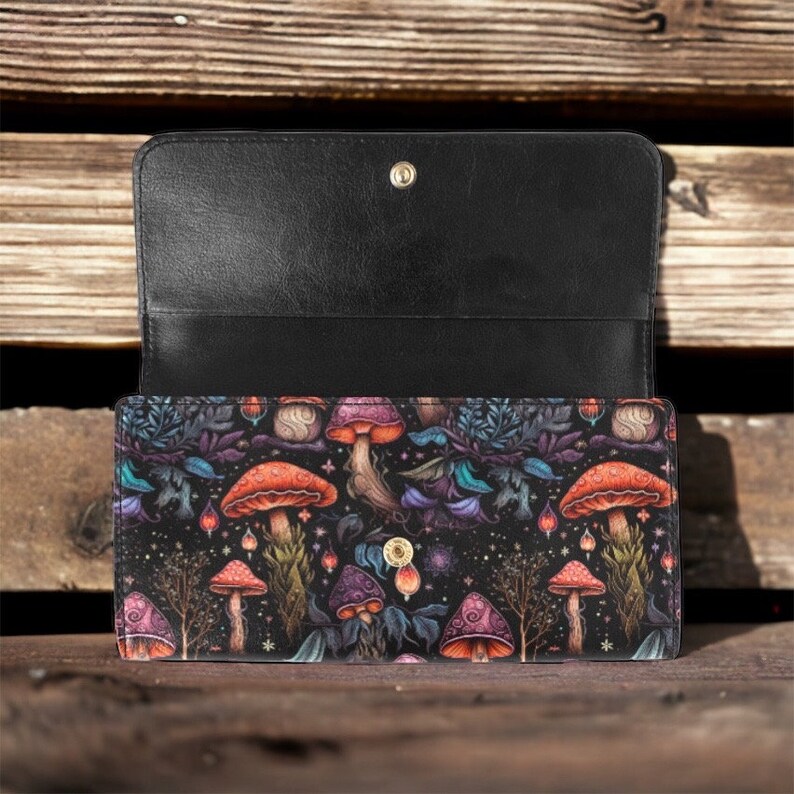 May include: A black leather wallet with a colorful mushroom print. The wallet has a flap closure and a snap button.