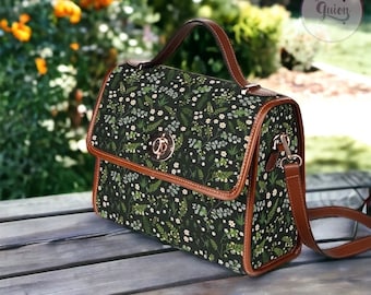 May include: A dark green satchel bag with a floral pattern and brown leather trim. The bag has a top handle and a long adjustable shoulder strap.