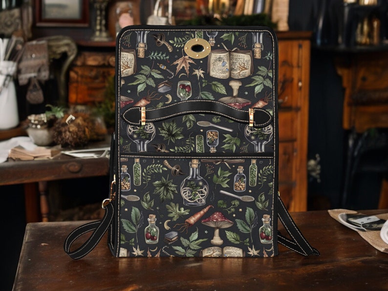May include: A black leather bag with a zipper closure and a long adjustable strap. The bag has a whimsical design featuring illustrations of herbs, potions, and other magical elements.