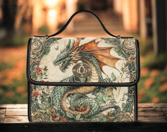 May include: A black-handled handbag featuring a detailed illustration of a dragon with green scales and orange wings. The bag has a black frame and a silver clasp. The dragon is set against a backdrop of flowers and foliage.