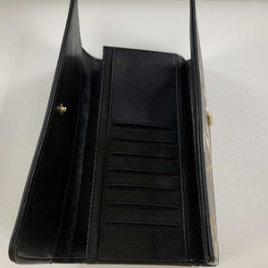 May include: Black leather wallet with multiple card slots and a billfold. The wallet is open and the interior is visible.