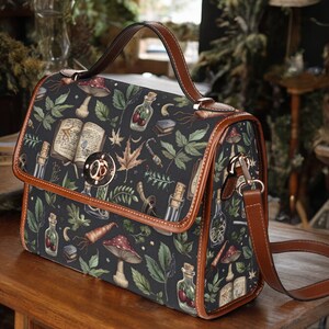 May include: A brown leather satchel with a black canvas body featuring a whimsical pattern of mushrooms, leaves, and potion bottles. The bag has a top handle and a long adjustable shoulder strap.